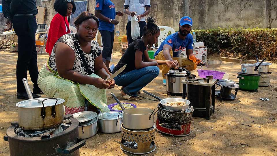 A woman cooking with biomass and an electric alternative in the background. 