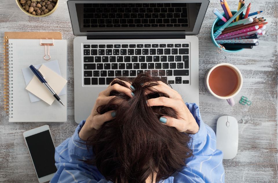 A woman at a office desk with her head in her hands 