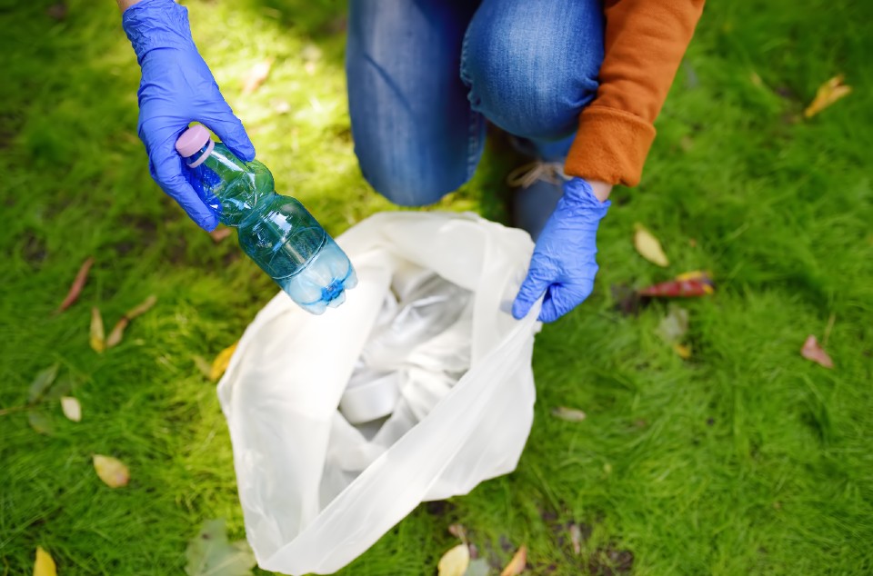 Man picking up litter from grass and putting it in bag. 