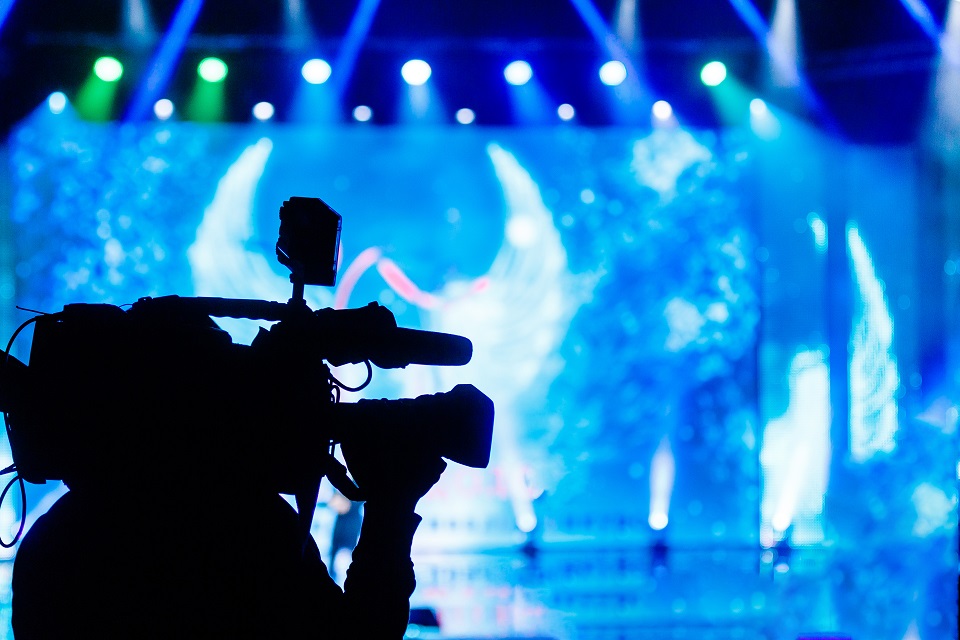 A camera operator is pictured in front of a blue stage