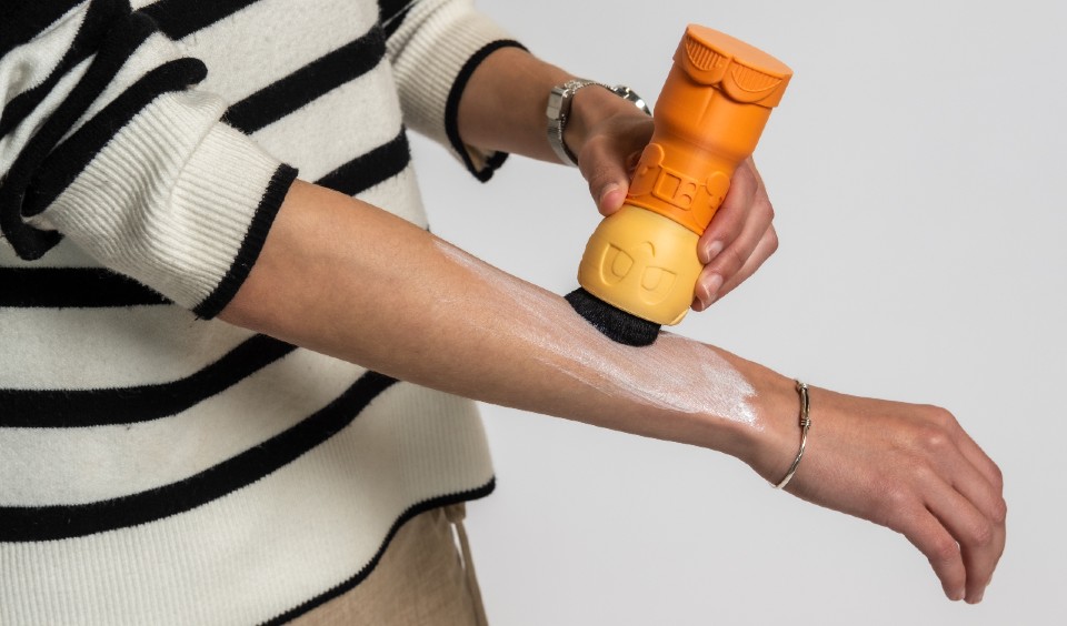 A woman applying suncream to her arm using the astronaut-shaped Sunny applicator 