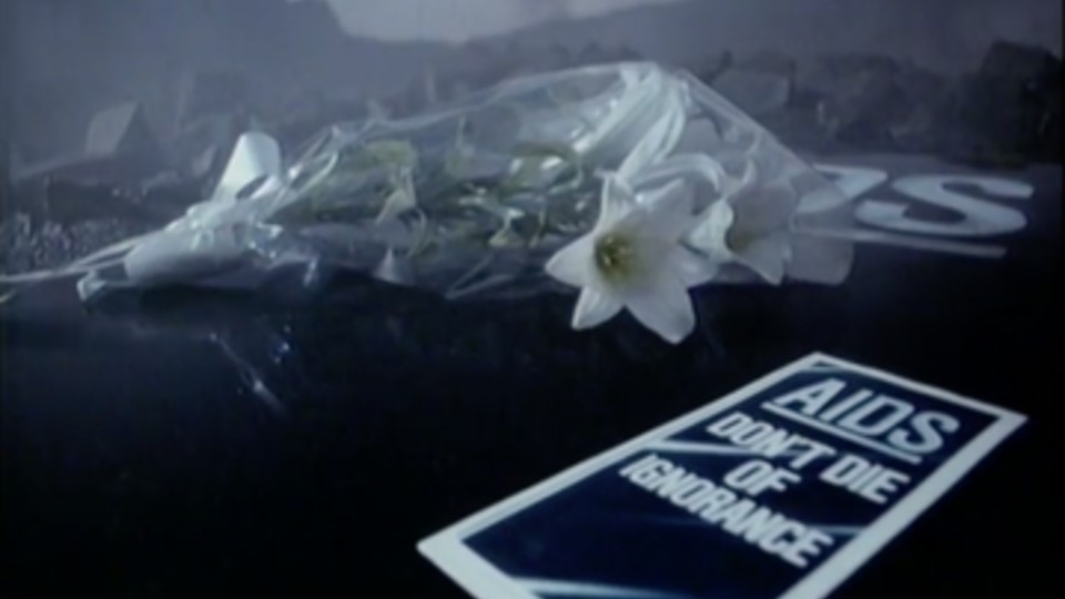 A bunch of flowers alongside a page reading 'AIDS don't die of ignorance'.