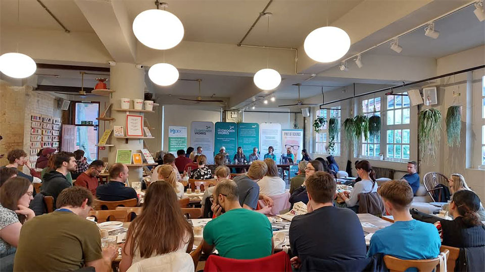 A large group of people seated at tables in a spacious room, engaged in conversation and activities.
