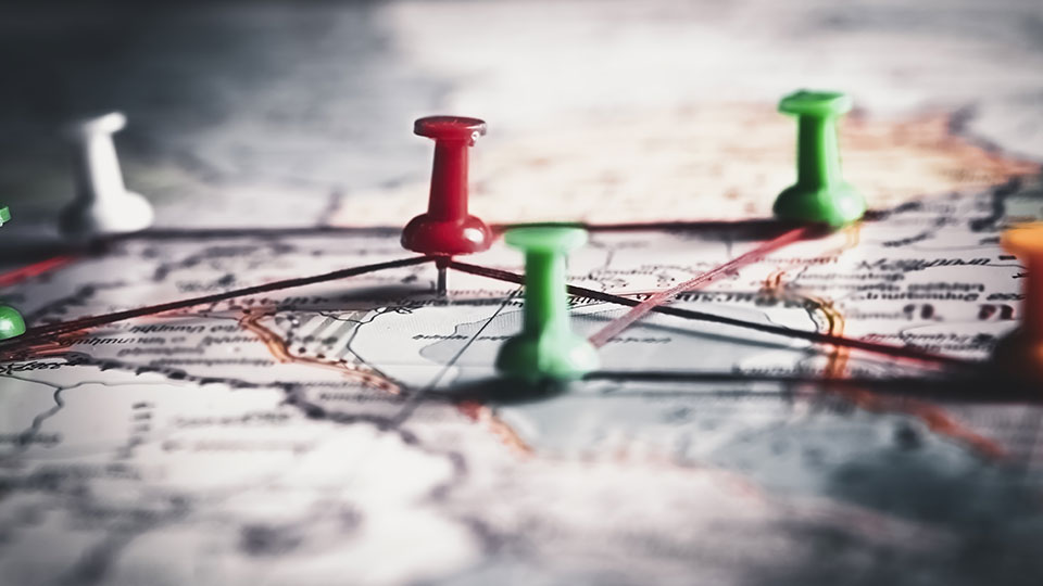 A map with green and red lips on certain locations and rubber bands connecting the pins.