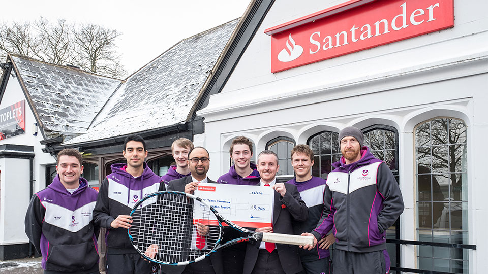 Tennis Foundation student volunteer coaches holding a cheque with some of the Loughborough University Santander branch staff