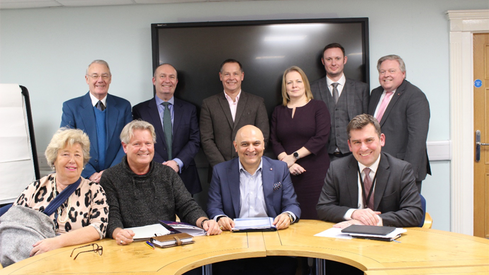 photo of members of the Loughborough Town Deal Board sat and stood around a table