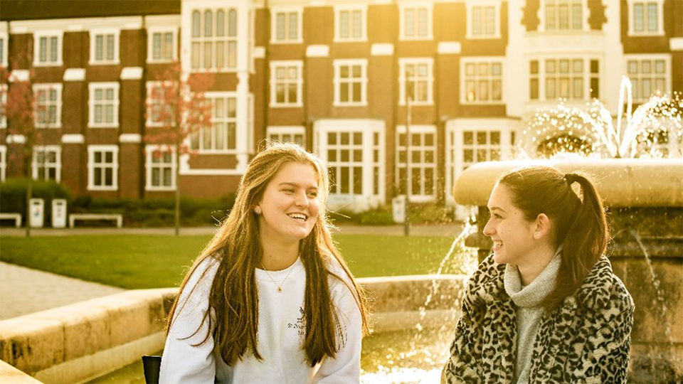 Photo of two students smiling and chatting sat by the Hazlerigg Rutland Fountain 