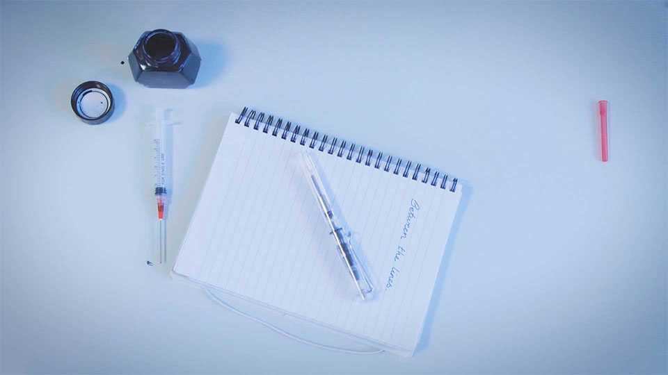 Photo of a notepad with 'Between the lines' written on and a pen and inkpot next to it