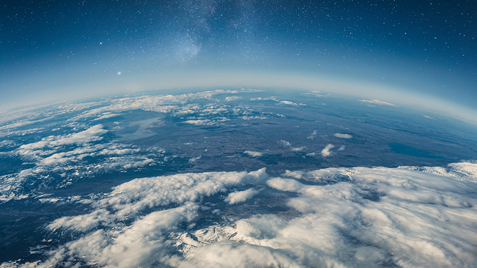Photo of a part of Earth from space, where you can see clouds and snow-topped mountains with a starry sky above it