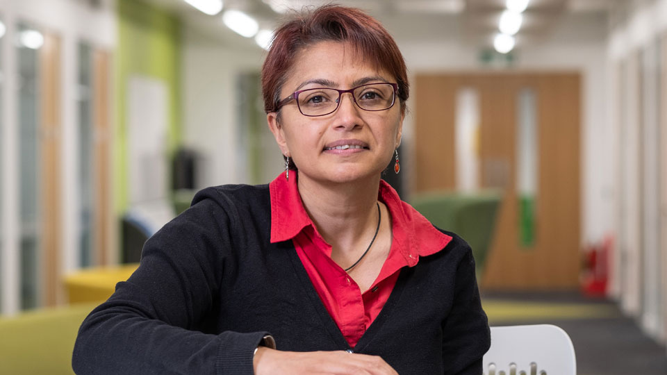 Photograph of Pooja Goddard, sitting in an open plan learning space