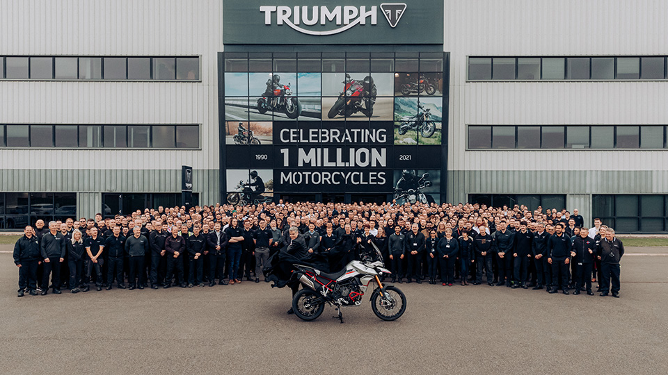 Photo of Triumph employees stood in front of building headquarters as well as one of their motorbikes, along with the banner "Celebrating 1 million motorcycles"