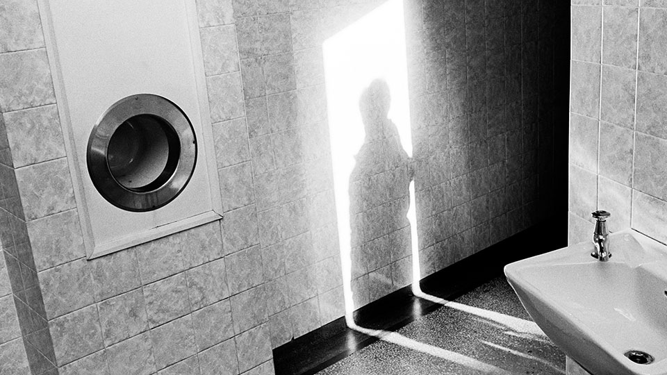 Black and white photo by Paul Hill with a sink and human shadow appearing in the light of a doorway