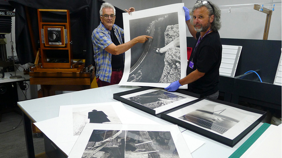 Photo of Alan Duncan and Paul Hill holding up a limited edition print over a table looking at the camera