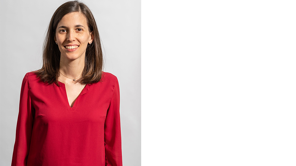 Image of Dr Ana facing the camera wearing a red shirt with a grey background behind her