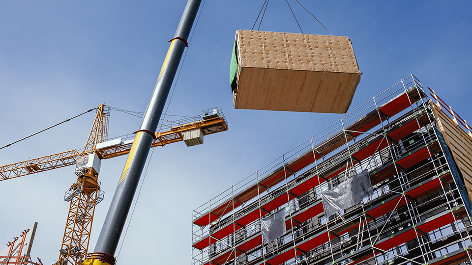 Photo of a building site with a crane and a timber modular being lifted into the air