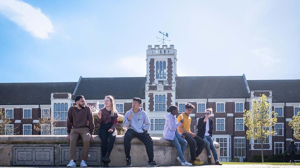 Photo of a group of students chatting together whilst sat on the fountain by the Hazlerigg and Rutland buildings