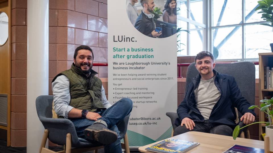 Image of two people sitting and smiling in front of LUinc. banner.