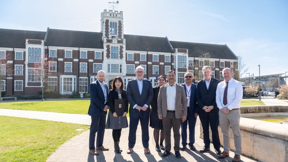 A photo of representatives from Loughborough University and SIU stood together outside the fountain in front of the Hazlerigg and Rutland buildings on campus during a sunny day.