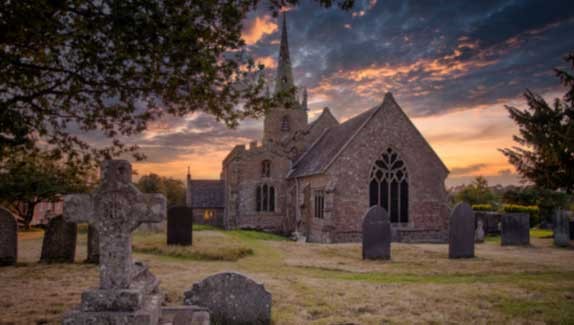 Front view of Peckleton Church, surrounding is grass, trees and gravestones.