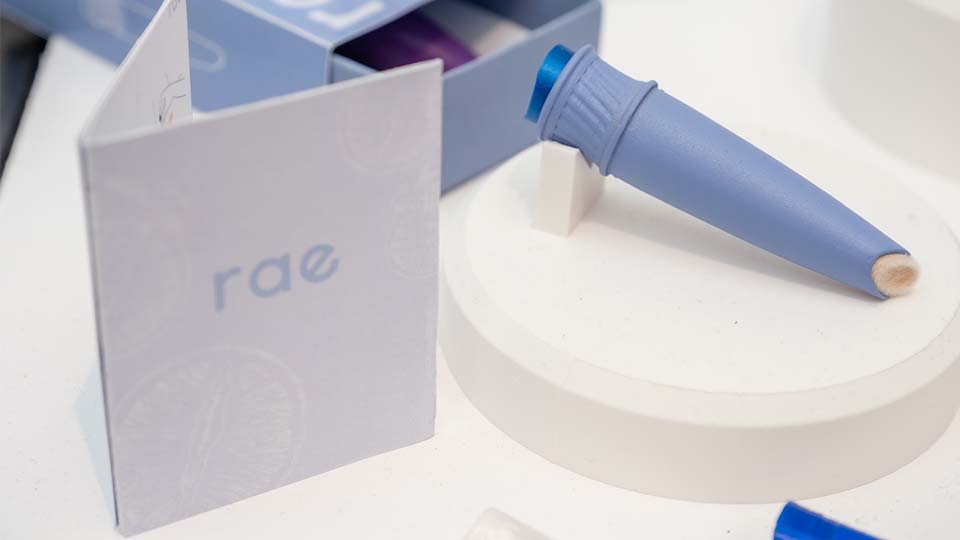 Close up of product prototype Rae, which is a purple plastic applicator with a swab on the end - with a leaflet card next to it