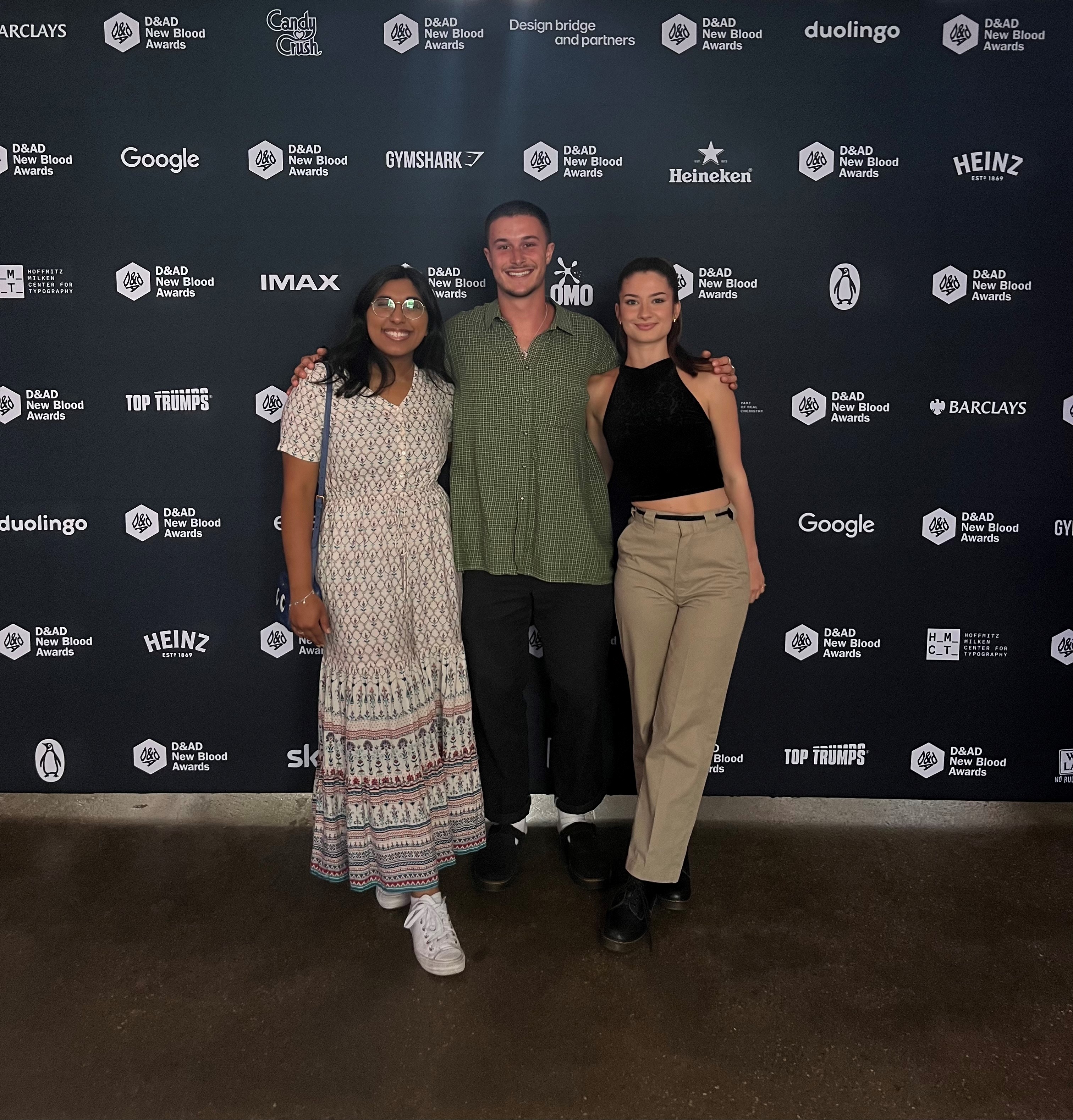 Graduates Nitya Thawani, David Hitchcock and Joanna Nicholl standing in front of a sponsored backdrop at the D&AD Awards evening.
