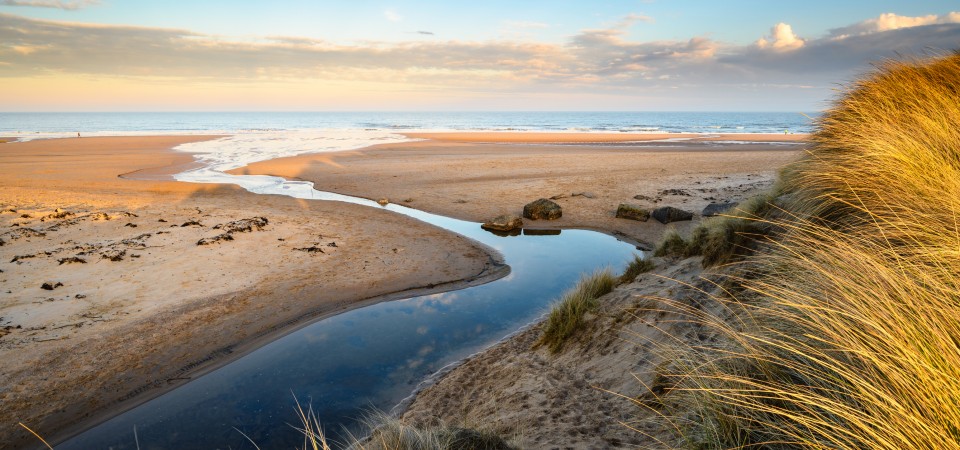 coastal sand dune with stream running through into the sea