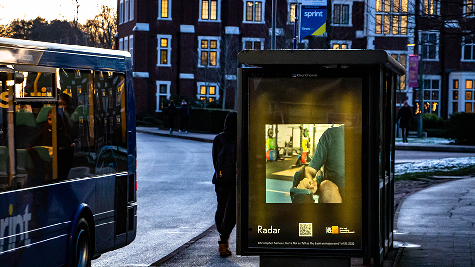 Photo of Christopher Samuel's photograph on a bus shelter poster on the Loughborough campus at dusk