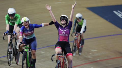 a cyclist celebrates a win with her hands in the air