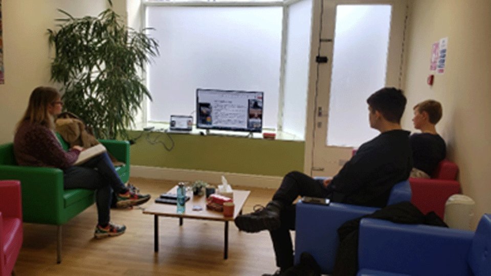 Three people sitting on sofas across a coffee table, watching a screen.