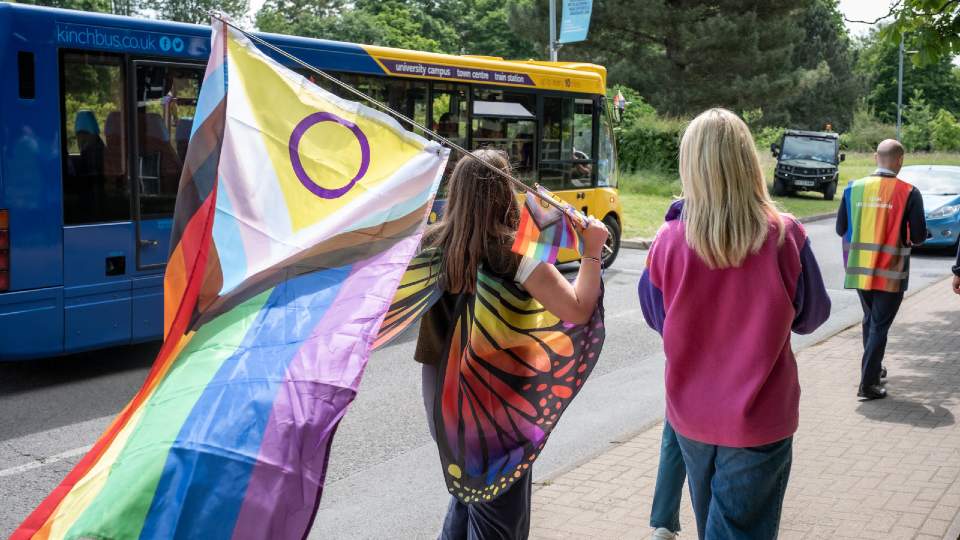 A group of people walking on campus during 2023 Pride March, one is wearing rainbow butterfly wings and carrying the LGBTQ+ flag.