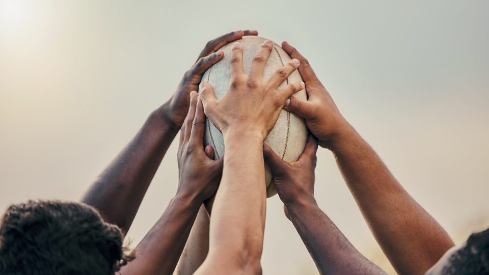 a number of humans collectively hold a rugby ball aloft