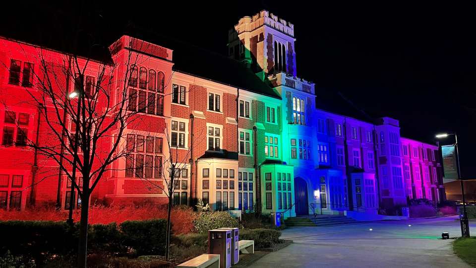 Hazlerigg Building on Loughborough campus lit up by rainbow coloured lights.