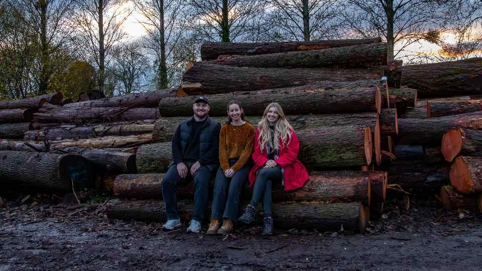 Fred, Chiara and Andrea sitting against a pile of logs in the woods.