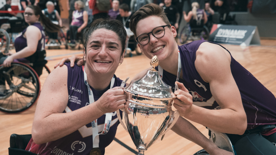 two basketball players pose with a trophy