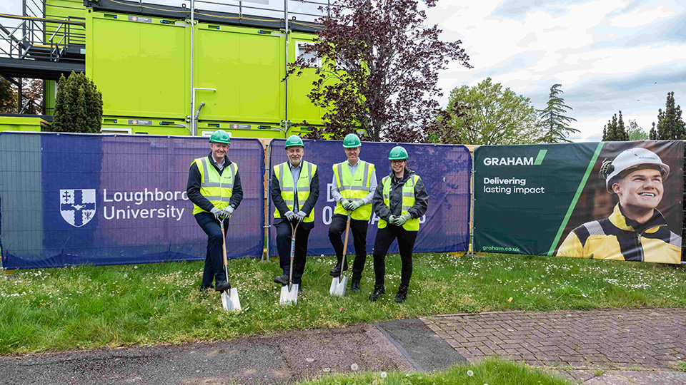 Four people wearing hi-vis jackets and green helmets standing outside of the new student accommodation development on campus.