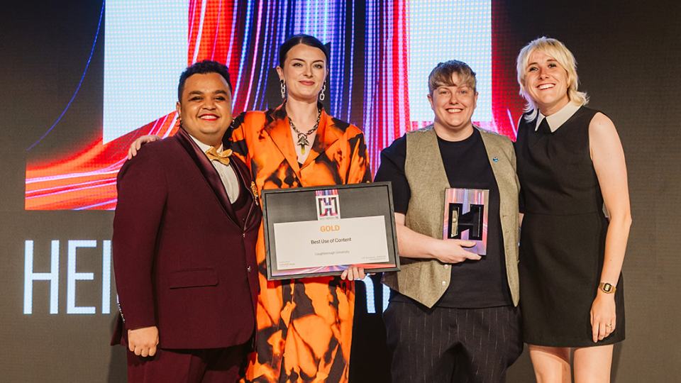 Two Loughborough colleagues standing on stage with two HEIST Award presenters, holding their HEIST trophy and certificate.