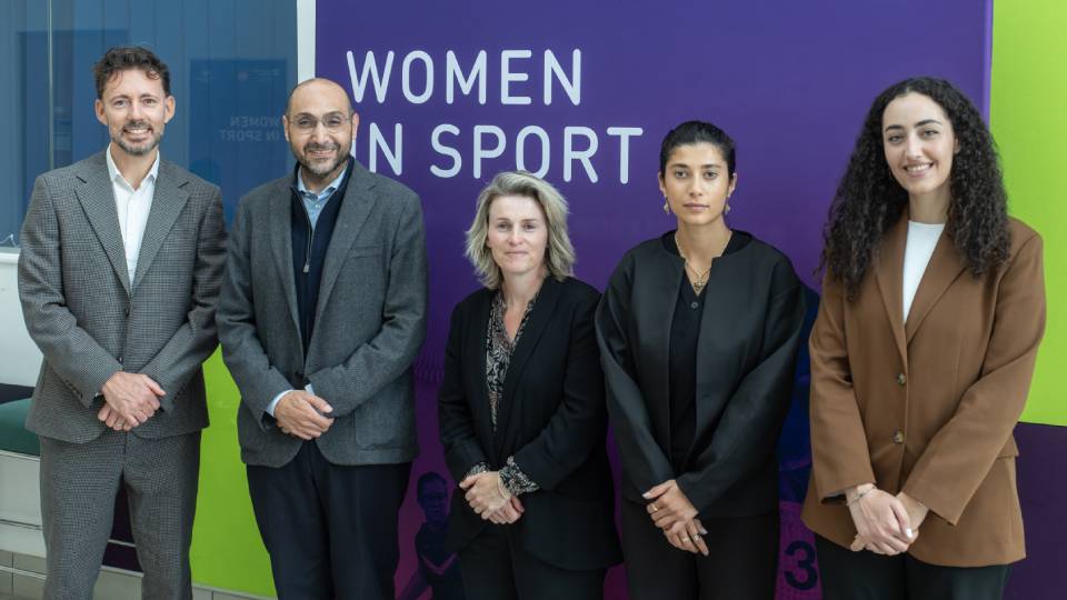 colleagues stood in front of a 'women in sport' sign