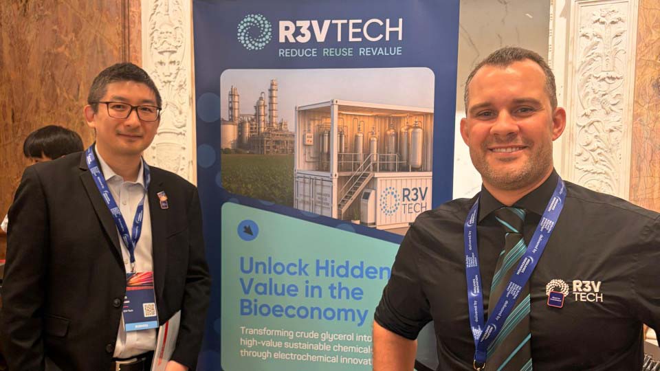 Two people wearing lanyards, standing alongside an R3VTech banner.