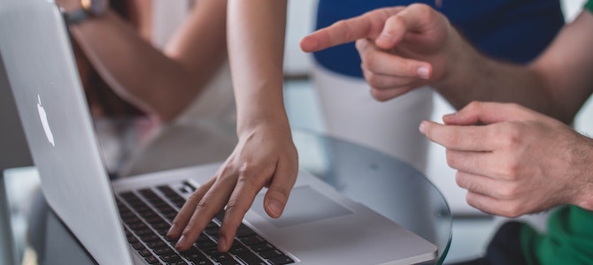 multiple hands pointing at and touching a laptop indicating a group project