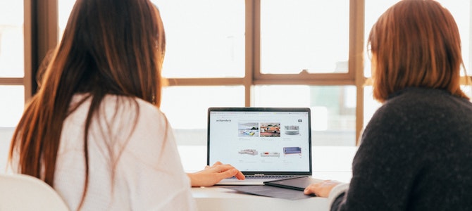 two women sat in front of a computer at a desk