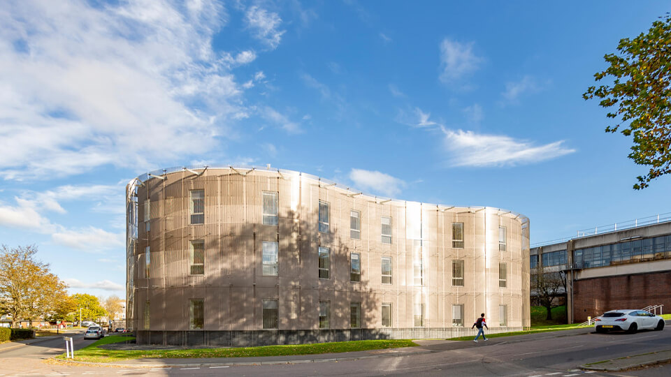 School of Architecture, Building and Civil Engineering building in the sunshine with a person walking across the street.