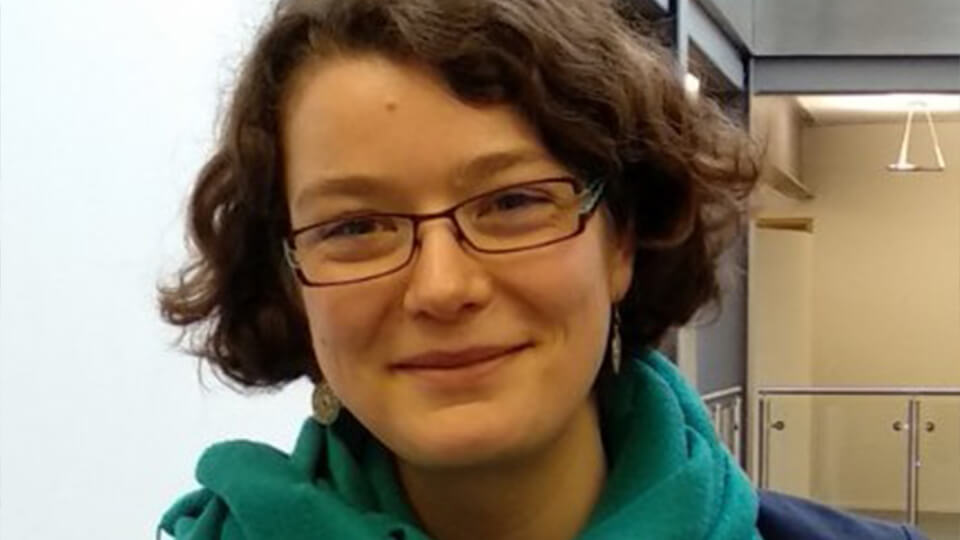 Female student with glasses and a scarf smiling directly at the camera.