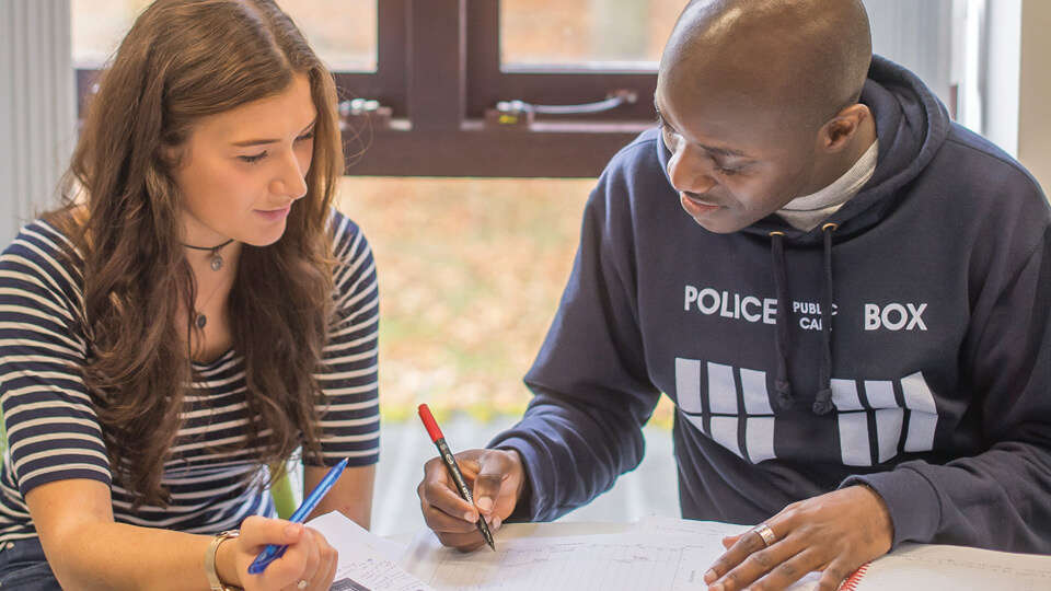 A male and a female student sat at a desk together, writing on pieces of paper.