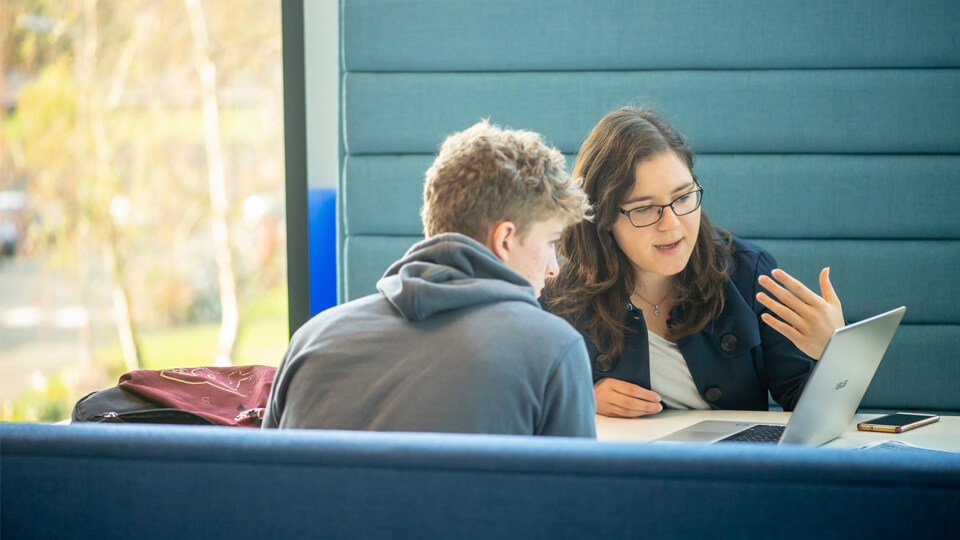 A member of staff and a student sitting at a desk in STEMLab while looking at a computer.