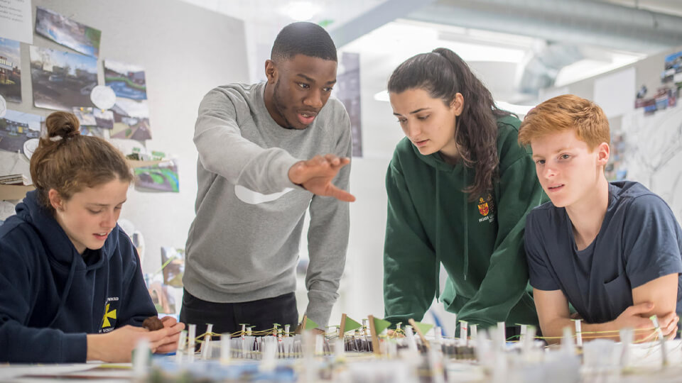Four students around a table discussing the small scale model on their table.