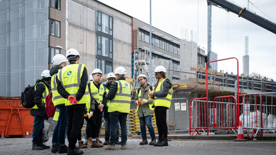 A group of students in high vis jackets and white helmets outside a Passivhaus building.