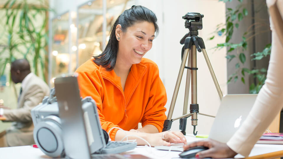 Female student smiling while speaking to another student in a well-lit study room.