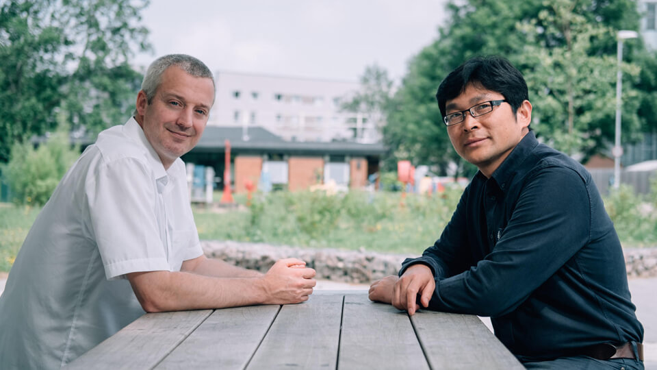 Two academics smiling to the camera while sitting outside on a picnic table across each other.