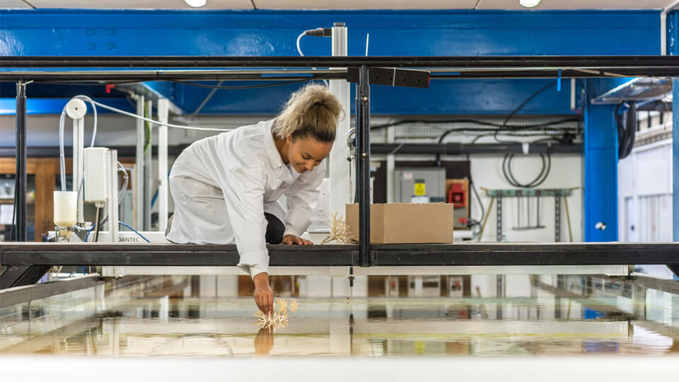 Female PhD Doctoral Researcher in the water flumes lab wearing a white lab coat.