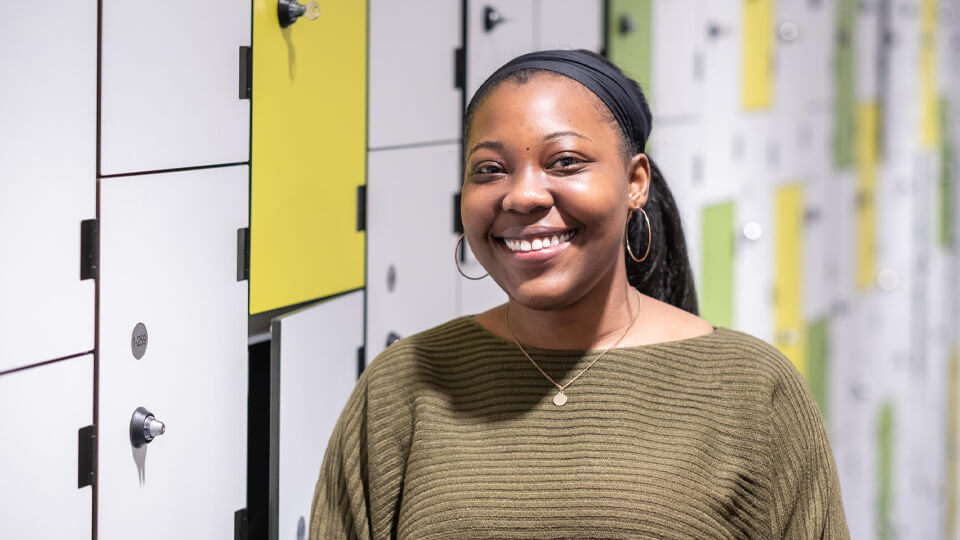 Student smiling at the camera indoors in the STEMLab with student lockers in the background.